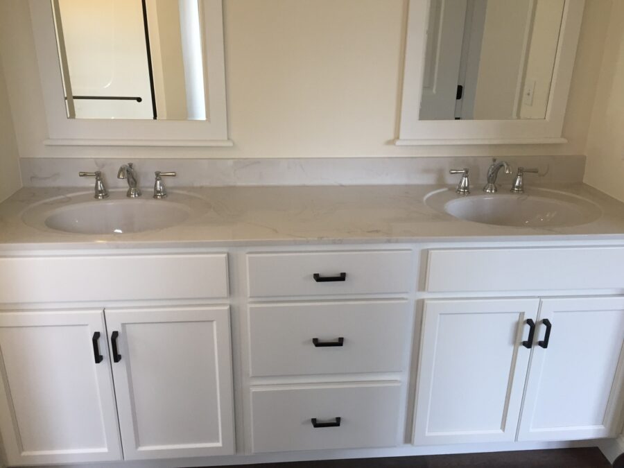 The Master Bathroom with white painted cabinetry with black hardware, cultured marble vanity tops and white-trim painted mirrors