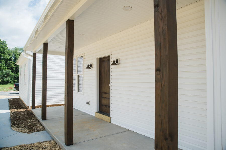 Full front porch with wood stained posts to match the stained front door on this custom home with white siding