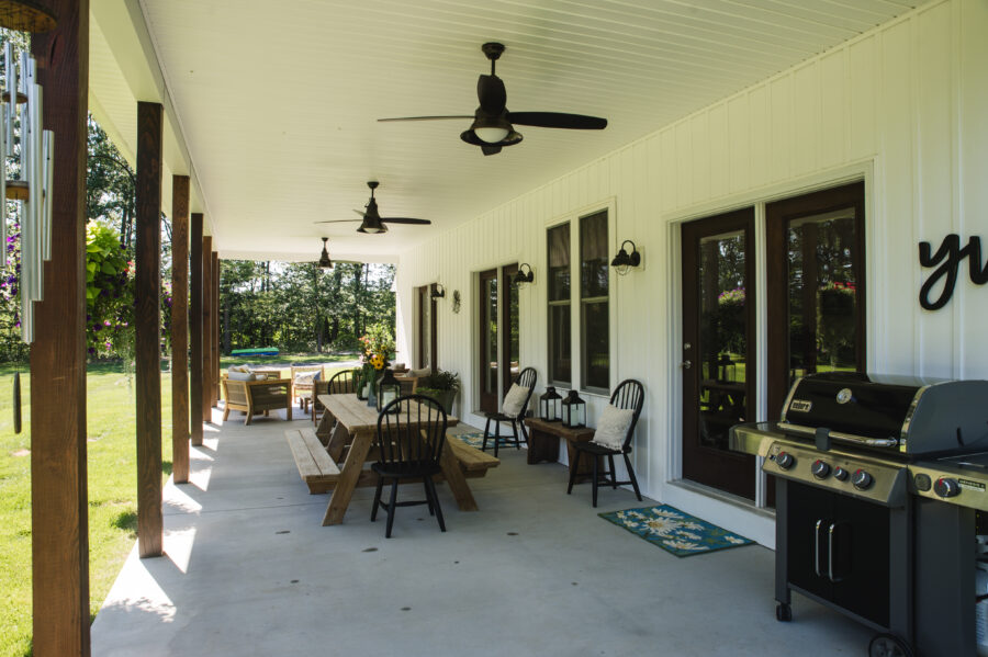 The rear covered porch with three sets of double patio doors, stained square porch posts, modern farmhouse exterior light fixtures and rustic furniture. 
