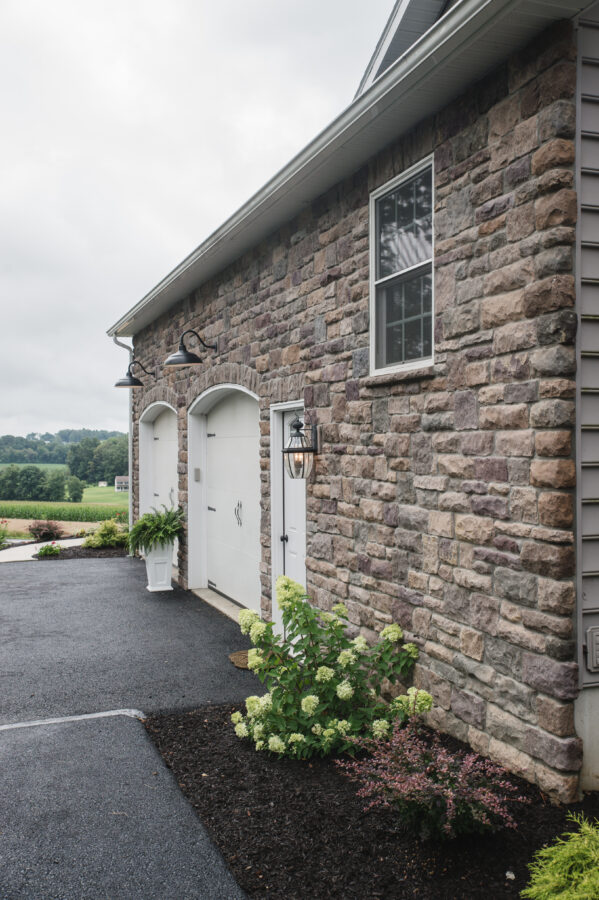 The side entry garage with arched openings at the garage door on a stone wall with a window. 