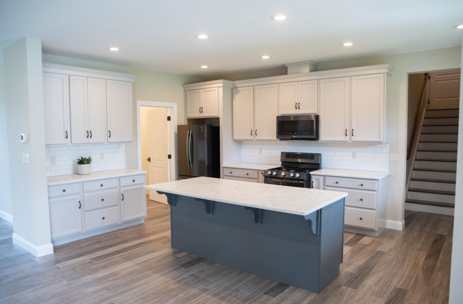 The open concept kitchen with white perimeter cabinets, a dark grey island, quartz countertops and simple subway tile backsplash. 