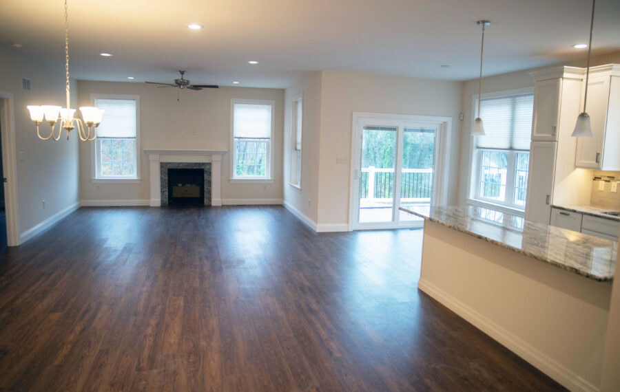 Open-concept great room, kitchen, and dining room with light beige walls and luxury vinyl plank flooring. 